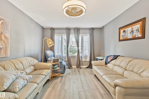 Living area featuring three large windows, wood-finish flooring, a contemporary ceiling light fixture, and neutral wall paint - 1619 Knottwood Road N, Edmonton, AB - Indoor Photo Showing Living Room