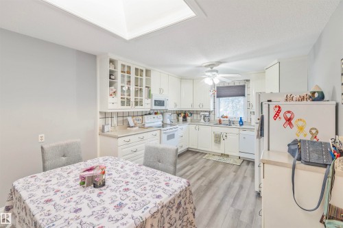 Bright kitchen featuring white cabinetry, light countertops, a ceiling fan, and wood-finish flooring - 1619 Knottwood Road N, Edmonton, AB - Indoor