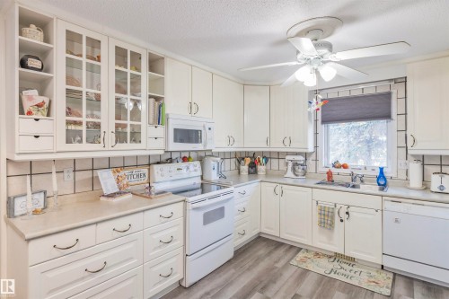 Kitchen featuring white cabinetry, light-toned countertops, a white tile backsplash with dark grout, wood-finish flooring, and a ceiling fan with integrated lighting - 1619 Knottwood Road N, Edmonton, AB - Indoor Photo Showing Kitchen