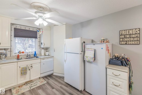 Kitchen featuring white cabinetry, wood-finish flooring, a ceiling fan with integrated lighting, a window with a roller shade, and white appliances - 1619 Knottwood Road N, Edmonton, AB - Indoor Photo Showing Kitchen
