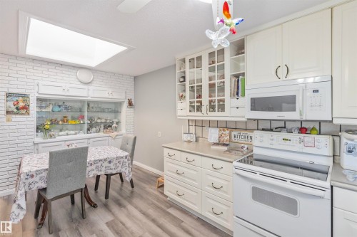 Kitchen featuring white cabinetry, a built-in microwave, a flat-top electric range, light-toned countertops, and wood-finish flooring - 1619 Knottwood Road N, Edmonton, AB - Indoor