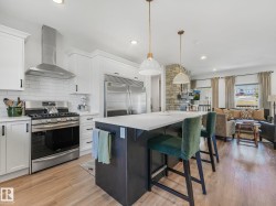 Open-concept kitchen featuring white shaker cabinetry, stainless steel appliances, white subway tile backsplash, a dark-toned kitchen island with seating, and wood-finish flooring - 