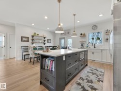 Spacious kitchen featuring a large central island with integrated microwave, pendant lighting, light wood-finish flooring, white perimeter cabinetry, and an undermount sink - 