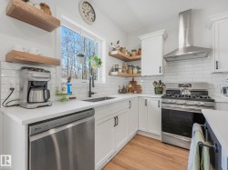 Modern kitchen featuring white shaker cabinetry, stainless steel appliances, wood-finish flooring, and open shelving - 