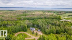 Expansive property featuring a two-story residence with a gray shingled roof, a detached auxiliary structure, extensive surrounding woodland, and a circular gravel driveway - 