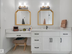 Contemporary vanity featuring white cabinetry with black hardware, a light-toned countertop, and two ornate gold-framed mirrors - 