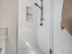 Shower with white subway tile walls, a built-in niche with wood-finish shelving, and matte black fixtures - 