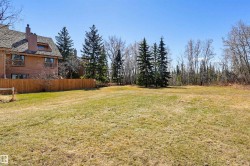 Expansive grassy area bordered by a wood fence and mature evergreen trees - 
