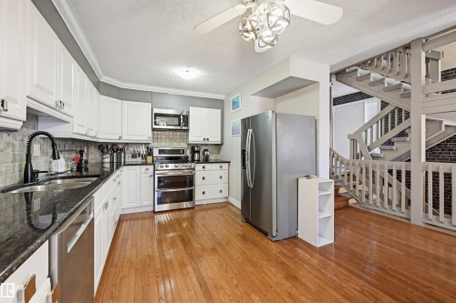Kitchen featuring wood-finish flooring, white cabinetry, dark countertops, and a full suite of stainless steel appliances - 139 Wolf Willow Crescent, Edmonton, AB - Indoor Photo Showing Kitchen With Double Sink