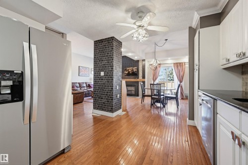 Open concept living space featuring wood-finish flooring, a kitchen with white cabinetry and dark countertops, a dining area with a modern light fixture, a brick-textured pillar, and a living area with a fireplace - 139 Wolf Willow Crescent, Edmonton, AB - Indoor Photo Showing Kitchen