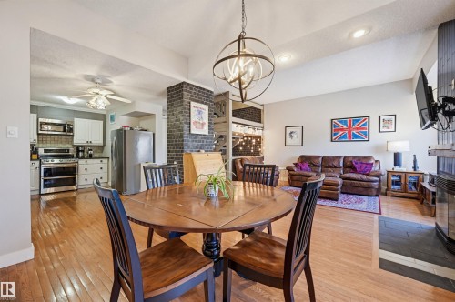Open concept interior featuring wood-finish flooring, a contemporary spherical chandelier, and a brick-finish accent pillar - 139 Wolf Willow Crescent, Edmonton, AB - Indoor Photo Showing Dining Room