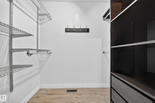 Organized closet space featuring wire shelving systems, dark wood-finish cabinetry with drawers, wood-finish flooring, and a wall-mounted rack - 1767 61 Street, Edmonton, AB - Indoor With Storage