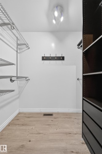 Walk-in closet featuring wood-finish flooring, white baseboards, a ceiling-mounted light fixture, metal wire shelving, and built-in dark wood cabinetry with drawers - 1767 61 Street, Edmonton, AB - Indoor With Storage