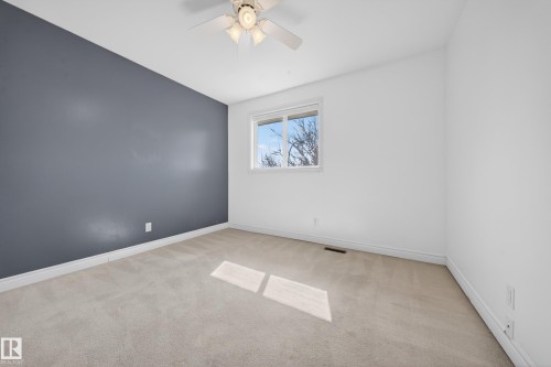 Spacious room featuring a white ceiling fan, light neutral carpeting, a large window, white baseboards, and a contrasting accent wall - 1767 61 Street, Edmonton, AB - Indoor Photo Showing Other Room