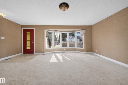 Spacious room featuring light-colored carpet flooring, a front entry door with decorative glass panels, and a prominent bay window with multiple panes - 1767 61 Street, Edmonton, AB - Indoor Photo Showing Other Room