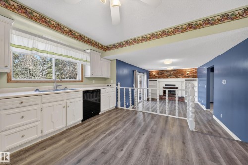 Bright kitchen featuring wood-finish flooring, white cabinetry with silver hardware, and a stainless steel sink with a gooseneck faucet - 1767 61 Street, Edmonton, AB - Indoor