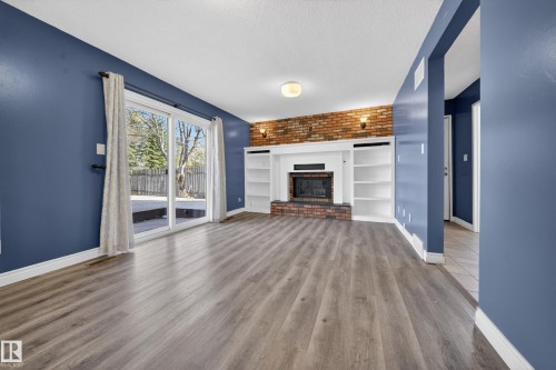 Living area featuring wood-finish flooring, a brick accent wall, built-in shelving, a fireplace with a white mantel, and sliding glass doors leading to an exterior deck - 1767 61 Street, Edmonton, AB - Indoor Photo Showing Living Room With Fireplace