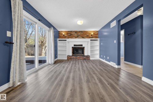 Spacious living area featuring wood-finish flooring, a brick fireplace with a white mantel, and built-in shelving - 1767 61 Street, Edmonton, AB - Indoor Photo Showing Living Room With Fireplace