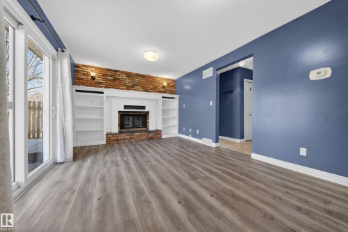 Spacious room featuring wood-finish flooring, a brick fireplace with a white mantle, and integrated built-in shelving - 1767 61 Street, Edmonton, AB - Indoor With Fireplace