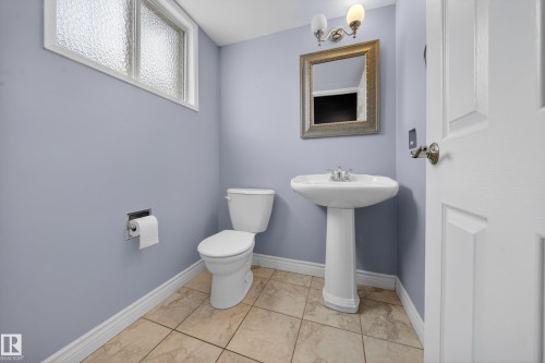 Bathroom featuring a pedestal sink, white toilet, tiled flooring, framed wall mirror, and a wall-mounted light fixture - 1767 61 Street, Edmonton, AB - Indoor Photo Showing Bathroom