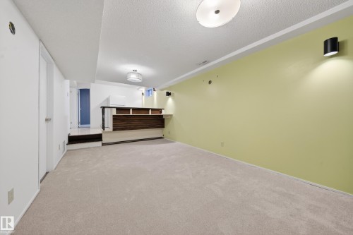 Spacious recreation room featuring light-colored carpeting, a built-in wet bar with dark wood-finish paneling, and a light green accent wall - 1767 61 Street, Edmonton, AB - Indoor Photo Showing Other Room
