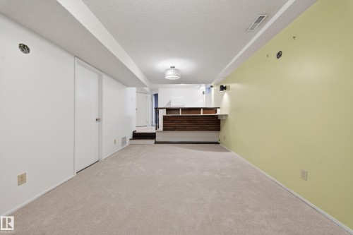 Finished lower level featuring neutral carpeting, recessed ceiling, recessed lighting, and a built-in bar with wood-finish paneling and an overhead light fixture - 1767 61 Street, Edmonton, AB - Indoor Photo Showing Other Room