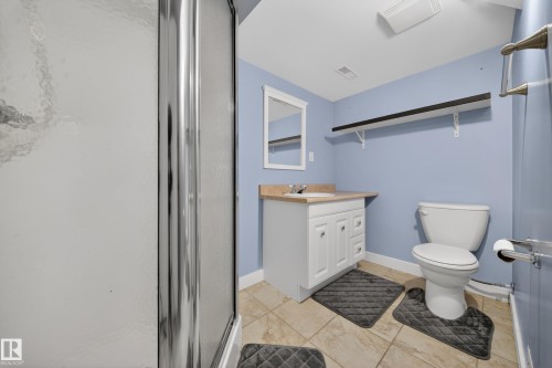 Bathroom featuring a stand-up shower with a textured glass enclosure, a white vanity with integrated sink, a light-colored countertop, and tiled flooring - 1767 61 Street, Edmonton, AB - Indoor Photo Showing Bathroom