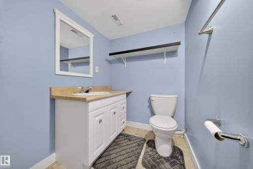 Bathroom featuring a single vanity with a white cabinet and neutral countertop, a white toilet, tiled flooring, and a wall-mounted mirror - 1767 61 Street, Edmonton, AB - Indoor Photo Showing Bathroom