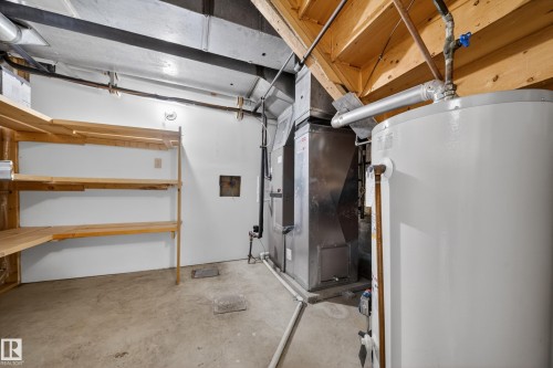 Utility room featuring a water heater, furnace, concrete flooring, exposed ceiling joists, and built-in wood shelving - 1767 61 Street, Edmonton, AB - Indoor
