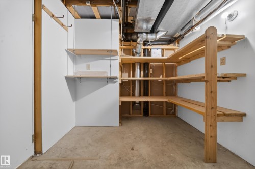 Unfinished basement storage area featuring concrete flooring, exposed ceiling joists, and integrated wood shelving - 1767 61 Street, Edmonton, AB - Indoor