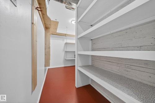 Storage area featuring built-in shelving with wood-look backing, red-toned flooring, white walls, and exposed wood beams - 1767 61 Street, Edmonton, AB - Indoor