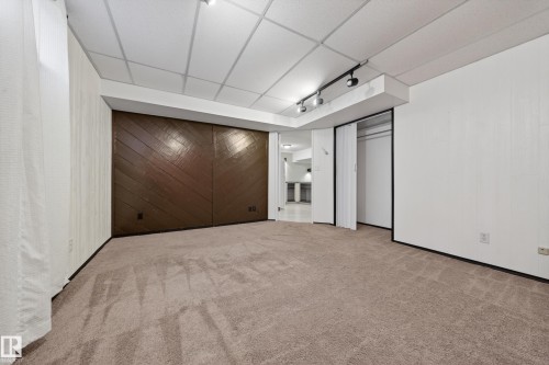 Carpeted room featuring a drop ceiling with recessed lighting, a brown wood-paneled accent wall, track lighting, and white walls - 1767 61 Street, Edmonton, AB - Indoor Photo Showing Other Room
