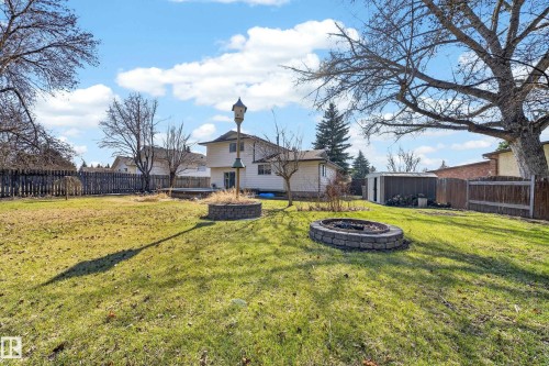 Expansive backyard featuring a manicured lawn, a stone-lined fire pit, a raised garden bed with stone surround, a utility shed, and mature trees - 1767 61 Street, Edmonton, AB - Outdoor