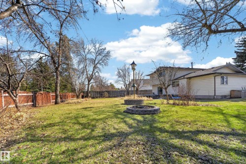 Expansive rear yard featuring a manicured lawn, two stone-clad fire pits, a tall birdhouse structure, a wood privacy fence, and mature trees - 1767 61 Street, Edmonton, AB - Outdoor