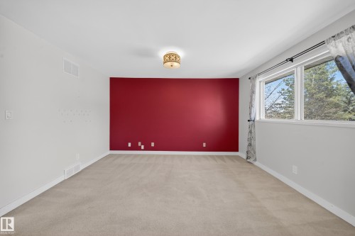 Spacious room featuring neutral carpeting, a distinctive accent wall, and multiple windows with outdoor scenery - 1767 61 Street, Edmonton, AB - Indoor Photo Showing Other Room