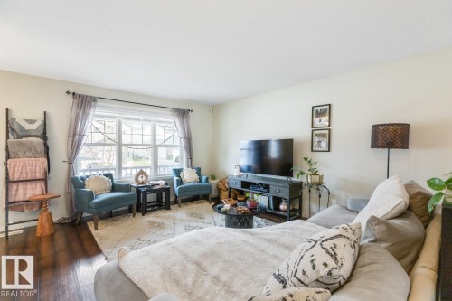 Bright living area featuring wood-finish flooring, a large multi-pane window, and light-toned walls - 5127 1A Avenue, Edmonton, AB - Indoor Photo Showing Living Room