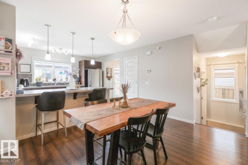 Open-concept living space featuring wood-finish flooring, a kitchen island with seating, pendant lighting, stainless steel appliances, and a tiled kitchen backsplash - 5127 1A Avenue, Edmonton, AB - Indoor Photo Showing Dining Room