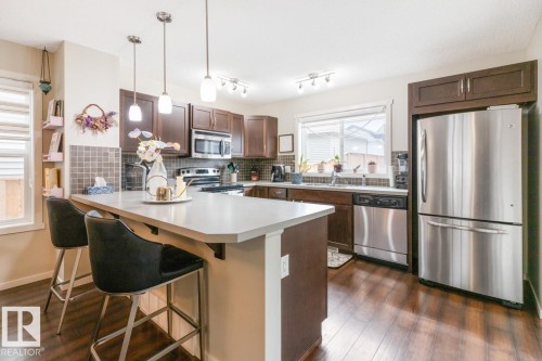 Kitchen featuring a central island with countertop seating, dark wood-finish cabinetry, stainless steel appliances, a tiled backsplash, and wood-finish flooring - 5127 1A Avenue, Edmonton, AB - Indoor Photo Showing Kitchen With Double Sink With Upgraded Kitchen