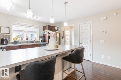 Kitchen featuring a spacious island with light-toned countertop, pendant lighting, dark wood-finish cabinetry, a window over the sink, and dark wood-finish flooring - 5127 1A Avenue, Edmonton, AB - Indoor