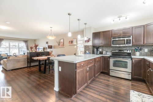 Kitchen featuring wood-finish flooring, dark wood cabinetry, stainless steel appliances, a tiled backsplash, and an island with pendant lighting - 5127 1A Avenue, Edmonton, AB - Indoor Photo Showing Kitchen