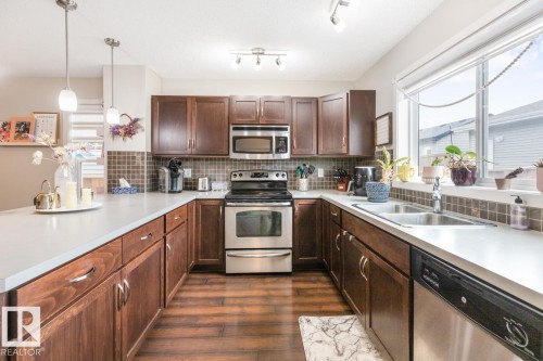 Kitchen featuring wood-finish flooring, dark wood cabinetry, white countertops, and a tiled backsplash - 5127 1A Avenue, Edmonton, AB - Indoor Photo Showing Kitchen With Double Sink