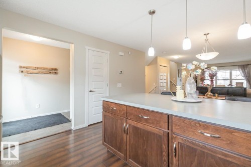 Kitchen island with wood-finish cabinetry, light-toned countertop, and three pendant lights - 5127 1A Avenue, Edmonton, AB - Indoor Photo Showing Kitchen