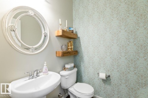 Pedestal sink with chrome faucet, complemented by a decorative round mirror - 5127 1A Avenue, Edmonton, AB - Indoor Photo Showing Bathroom