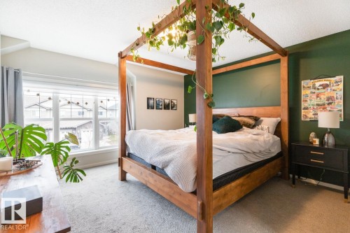 Carpeted room featuring a large window with white trim, a dark green accent wall, and a sloped ceiling - 5127 1A Avenue, Edmonton, AB - Indoor Photo Showing Bedroom