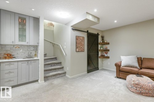 Finished lower level offering a wet bar with shaker cabinetry and stone backsplash, recessed lighting, carpeted flooring, a barn door, and a staircase with carpeted treads and a handrail - 5127 1A Avenue, Edmonton, AB - Indoor