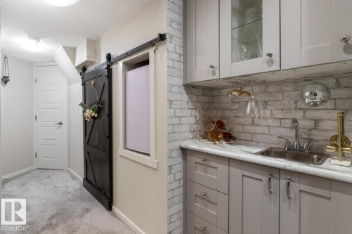 Wet bar featuring light gray cabinetry, a stainless steel sink with a chrome faucet, and a stone-finish countertop - 5127 1A Avenue, Edmonton, AB - Indoor Photo Showing Kitchen