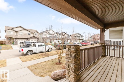 Inviting front porch featuring wood-finish decking, dark brown railings, and stone-clad pillars - 5127 1A Avenue, Edmonton, AB - Outdoor With Deck Patio Veranda