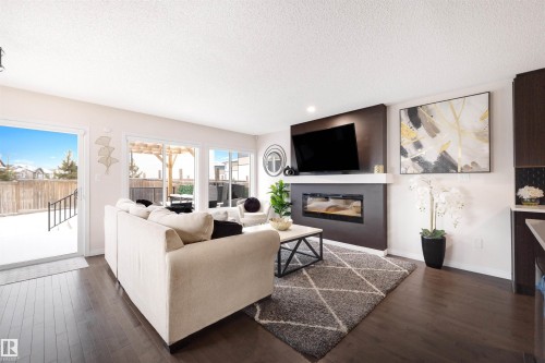 Living area featuring wood-finish flooring, a contemporary fireplace with a dark surround, and large sliding glass doors providing access to the outdoor space - 2504 Coughlan Road, Edmonton, AB - Indoor Photo Showing Living Room With Fireplace
