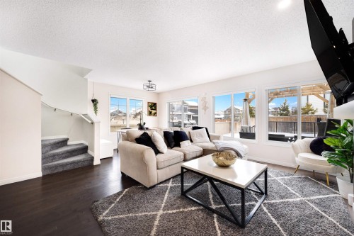 Open-concept living area featuring dark wood-finish flooring, a wall of large windows, and a staircase with plush gray carpeting - 2504 Coughlan Road, Edmonton, AB - Indoor Photo Showing Living Room