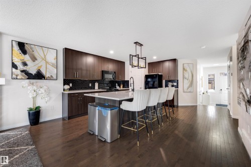 Spacious kitchen featuring an expansive island with seating, dark wood-finish cabinetry, black tile backsplash, and dark wood-finish flooring - 2504 Coughlan Road, Edmonton, AB - Indoor Photo Showing Kitchen